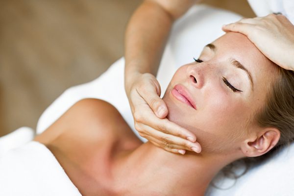 Young blond woman receiving a head massage in a spa center with eyes closed. Female patient is receiving treatment by professional therapist.